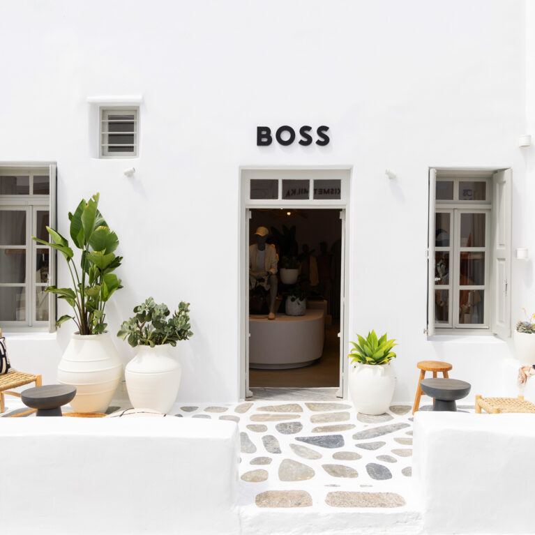 The entrance to the Boss pop-up store in Mykonos exudes a sophisticated yet relaxed aesthetic. The crisp white façade, stone-paved patio, and natural textures create a harmonious balance between Cycladic tradition and modern elegance, welcoming visitors into a refined retail experience.