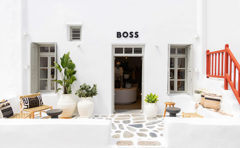 The entrance to the Boss pop-up store in Mykonos exudes a sophisticated yet relaxed aesthetic. The crisp white façade, stone-paved patio, and natural textures create a harmonious balance between Cycladic tradition and modern elegance, welcoming visitors into a refined retail experience.