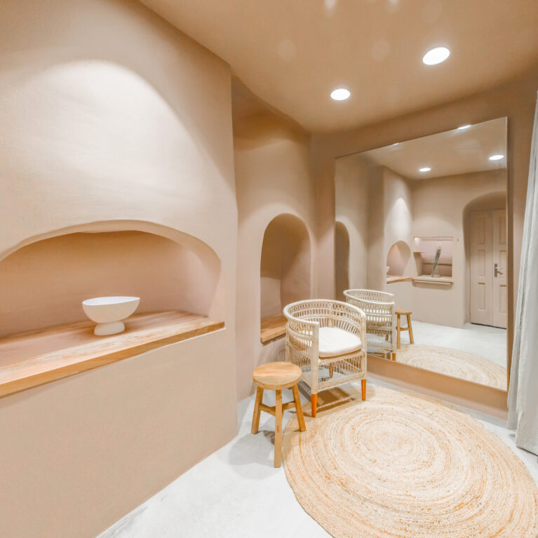 A soothing blend of soft, organic curves and natural textures creates a calming atmosphere in the boutique’s fitting area. The space is designed for comfort, with neutral hues, handcrafted elements, and warm lighting enhancing the overall sensory experience.