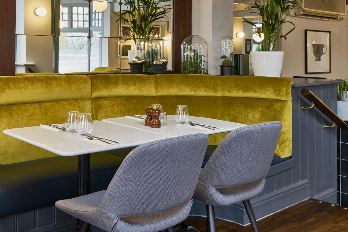 A dining corner featuring olive green velvet seating and grey upholstered chairs.