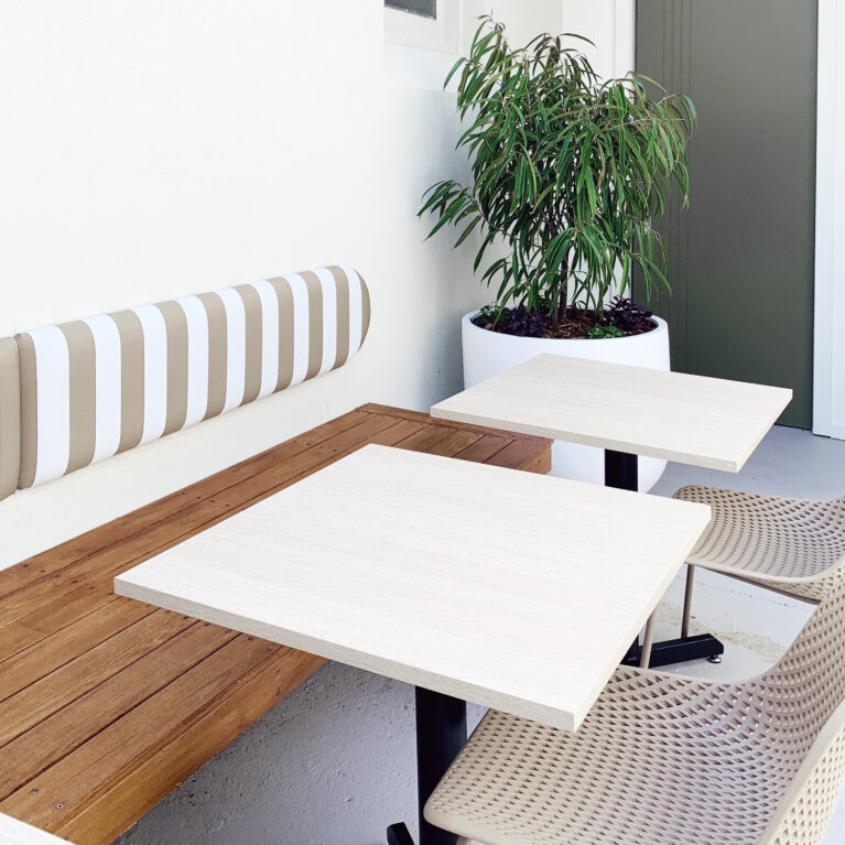 Sofia’s courtyard seating embraces natural textures and soft tones. Striped upholstery, blonde wood tables, and green potted plants create a relaxing escape, blending modern urban design with a welcoming outdoor retreat.