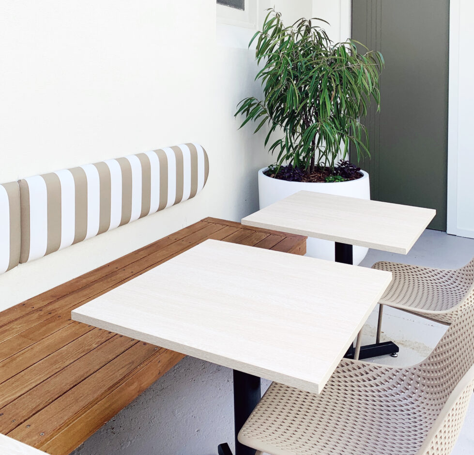 Sofia’s courtyard seating embraces natural textures and soft tones. Striped upholstery, blonde wood tables, and green potted plants create a relaxing escape, blending modern urban design with a welcoming outdoor retreat.