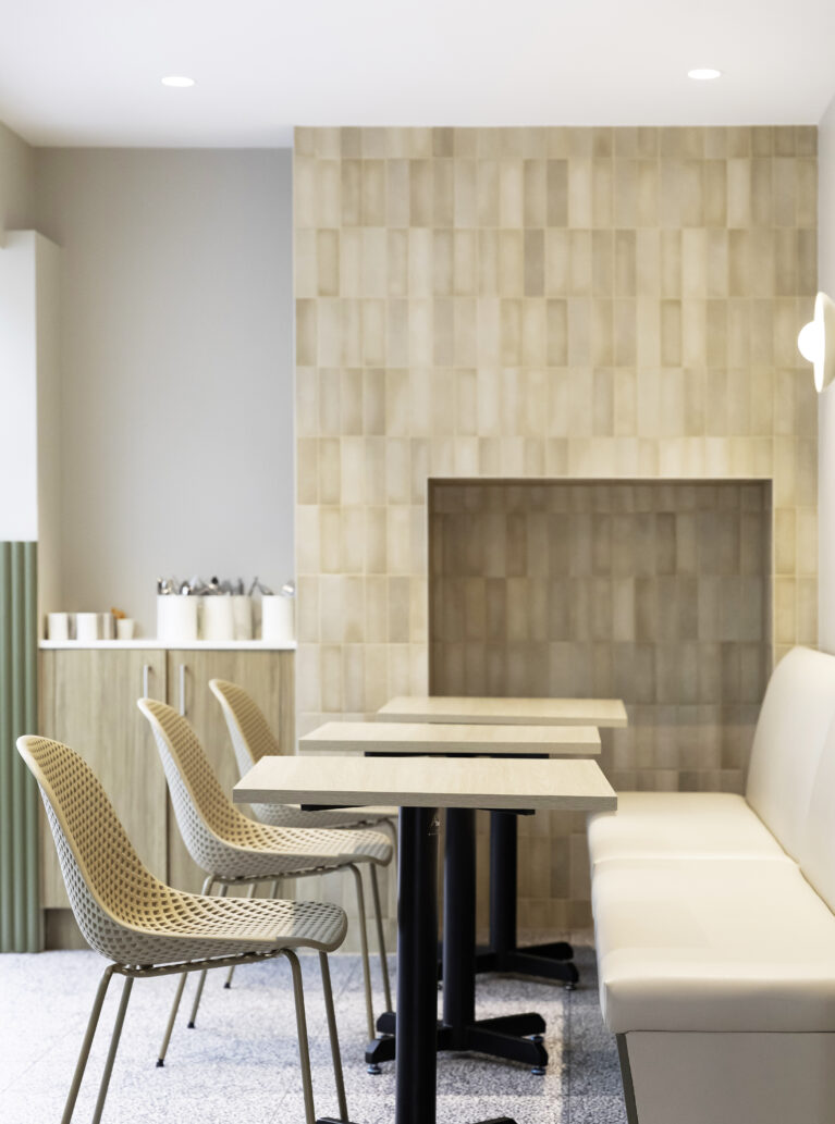 Sofa’s dining area features a neutral palette with soft beige tiles and minimalist furniture. Light wood tables and woven chairs bring warmth, while clean lines enhance the modern, inviting ambiance.