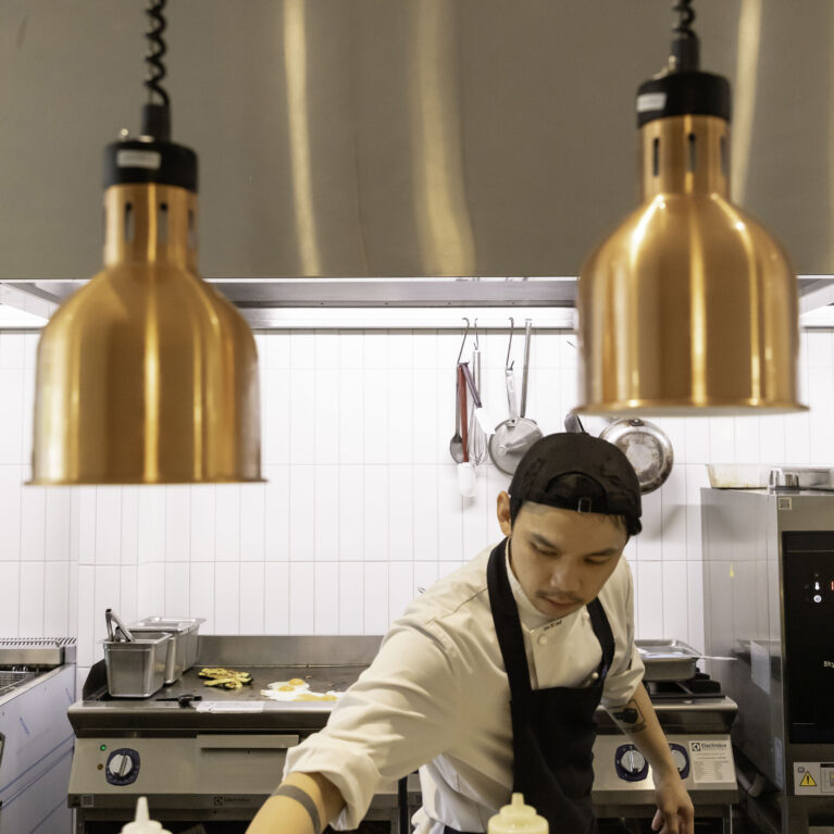 Sofia’s open kitchen highlights craftsmanship and transparency. Warm copper lighting contrasts with sleek stainless steel, reflecting the café’s blend of rustic and modern design elements.