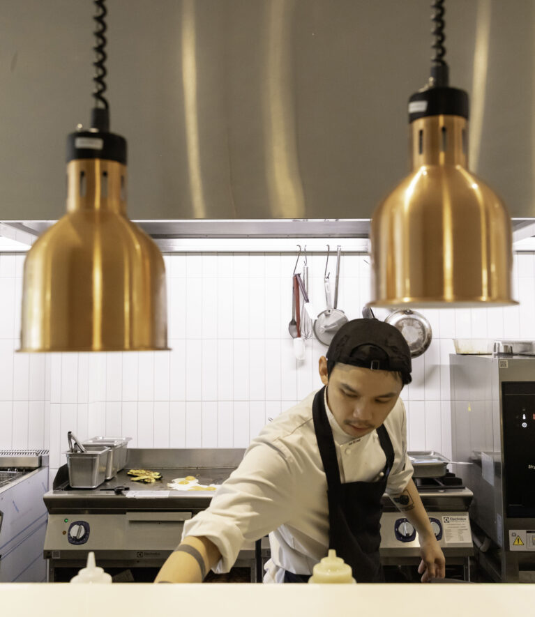 Sofia’s open kitchen highlights craftsmanship and transparency. Warm copper lighting contrasts with sleek stainless steel, reflecting the café’s blend of rustic and modern design elements.