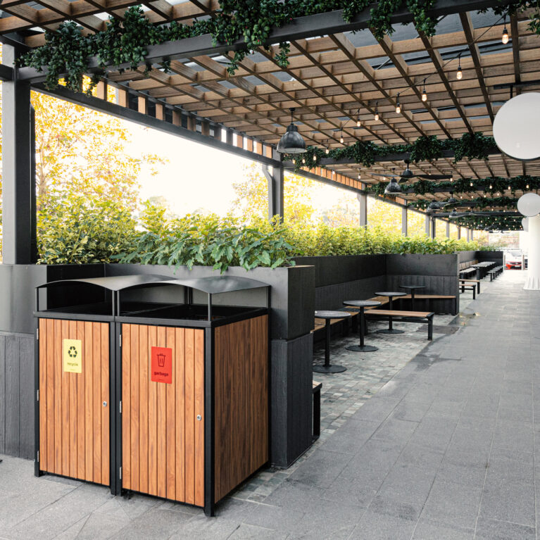 Timber clad bin enclosure, recycling station, steel arbour framework, timber lattice ceiling, outdoor dining concourse, grey stone paving, stainless steel bollard, perimeter planter boxes, festoon lighting, Sydney retail precinct.