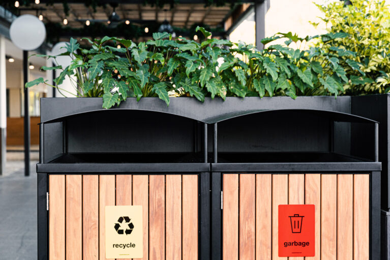 Timber slat bin enclosure, custom waste management station, black steel framing, recycling signage, integrated planter box, tropical landscaping, public amenity design, Sydney commercial fitout, sustainable precinct design.