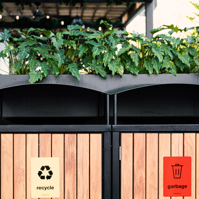 Timber slat bin enclosure, custom waste management station, black steel framing, recycling signage, integrated planter box, tropical landscaping, public amenity design, Sydney commercial fitout, sustainable precinct design.