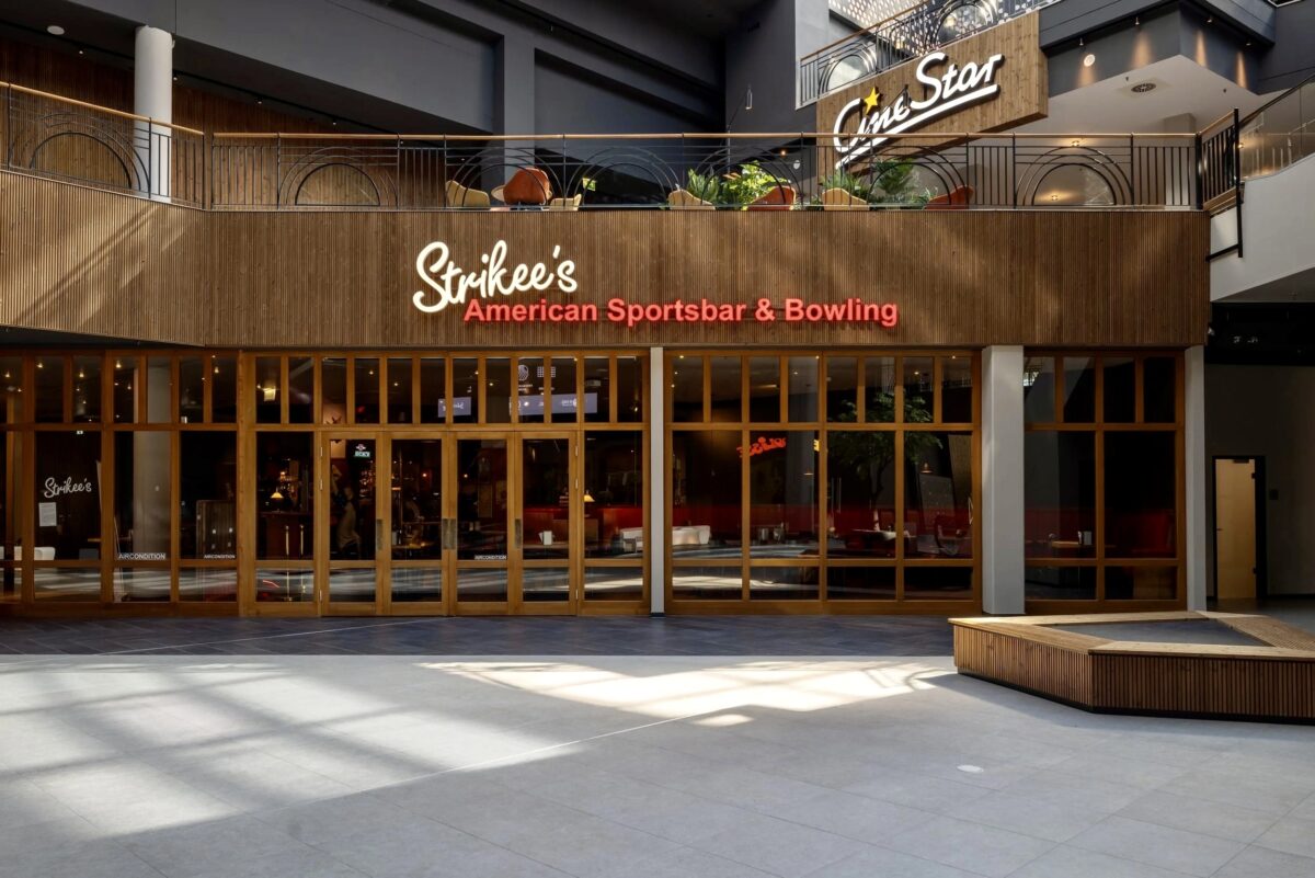 Hospitality storefront architecture, timber frame glazing, custom wooden paneling, commercial neon sign, sports bar entrance, mezzanine floor alignment, large format ground tile, integrated venue branding.