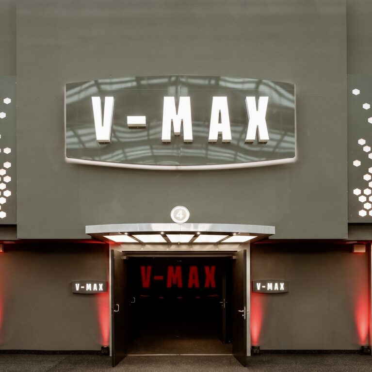 Auditorium entrance portal, backlit cinema marquee, perforated metal cladding, textured charcoal plaster, theatrical light canopy, symmetrical double doors, red ambient wall wash, premium theater branding.