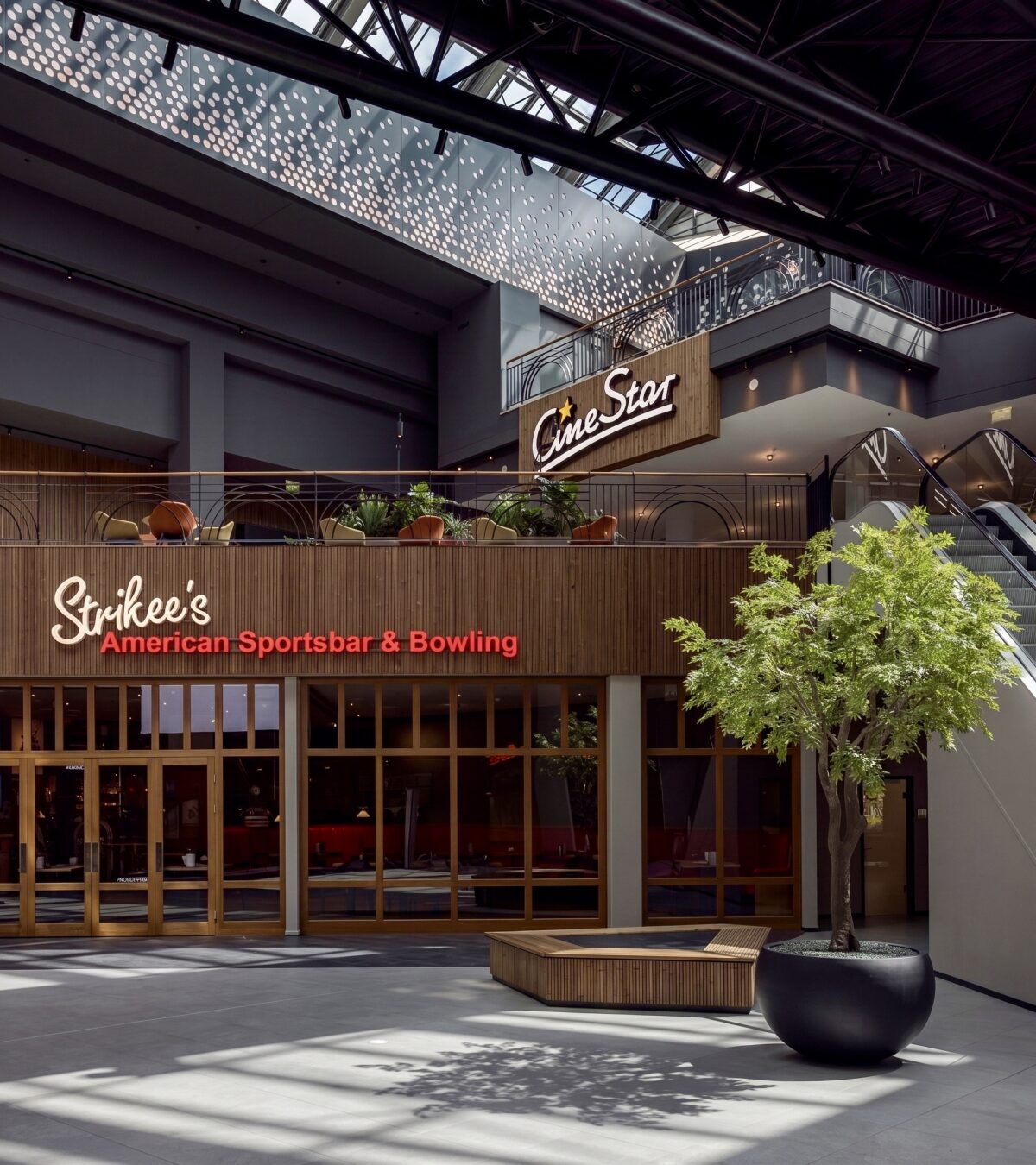 Indoor plaza layout, architectural planter seating, commercial timber framing, multi-level facade alignment, illuminated brand signage, dark steel roof truss, large format floor tiling, landscape interior accents.