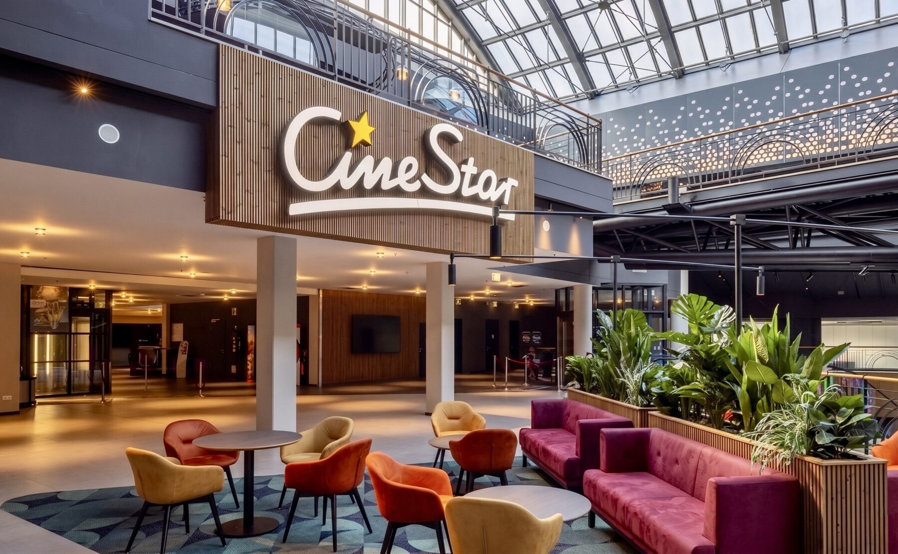 Cinema brand signage, vertical wood slat wall, hospitality waiting lounge, velvet cluster seating, commercial planter boxes, skylight illuminated lobby, architectural glass canopy, theater mezzanine corridor.