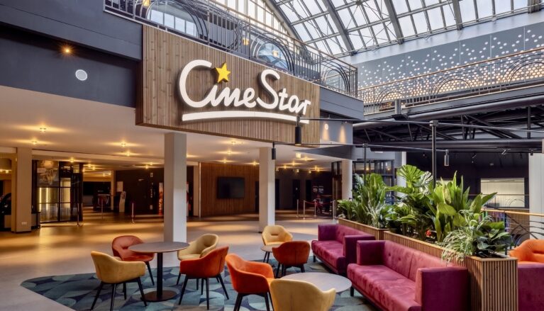 Cinema brand signage, vertical wood slat wall, hospitality waiting lounge, velvet cluster seating, commercial planter boxes, skylight illuminated lobby, architectural glass canopy, theater mezzanine corridor.