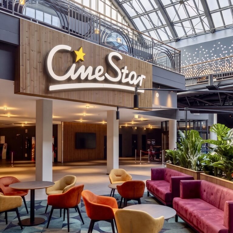 Cinema brand signage, vertical wood slat wall, hospitality waiting lounge, velvet cluster seating, commercial planter boxes, skylight illuminated lobby, architectural glass canopy, theater mezzanine corridor.