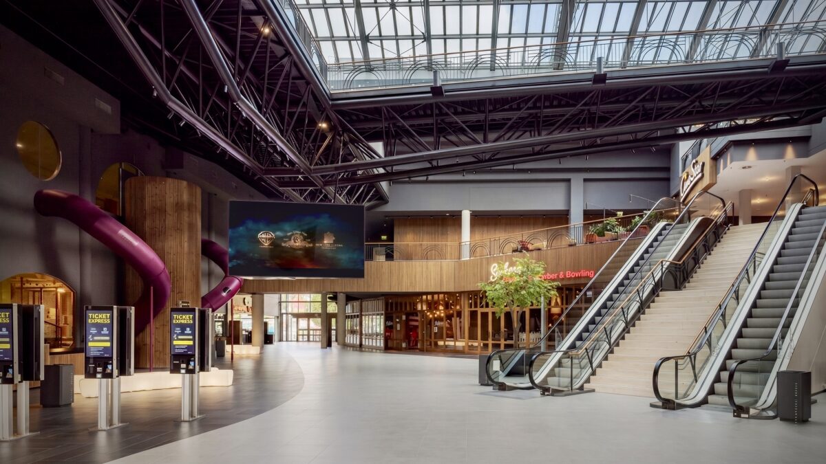 Cinema entry foyer, dual commercial escalators, industrial steel roof truss, architectural timber cladding, self-service ticketing kiosks, large format digital signage, indoor playground slides, open plan transit layout.