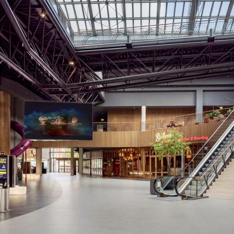 Cinema entry foyer, dual commercial escalators, industrial steel roof truss, architectural timber cladding, self-service ticketing kiosks, large format digital signage, indoor playground slides, open plan transit layout.