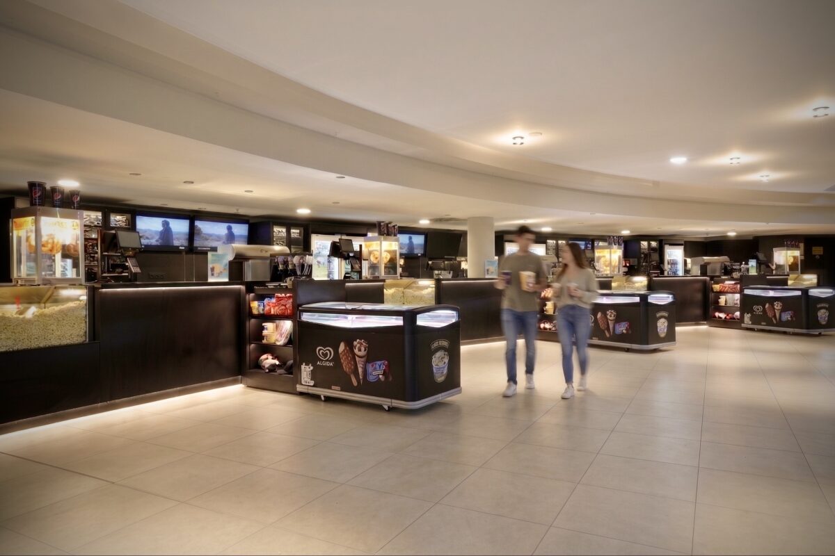 Cinema concession stand, theater candy counter, sleek food service joinery, curved ceiling bulkheads, linear led under-counter lighting, large format floor tiles, digital menu boards, refreshment zone design