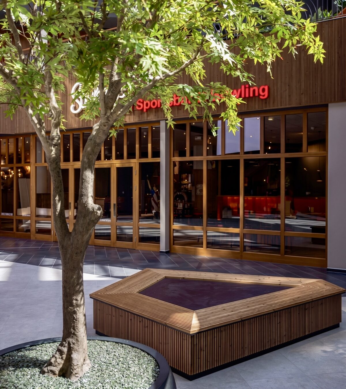 Custom timber bench, biophilic interior architecture, indoor tree planter, commercial plaza courtyard, timber frame storefront, hospitality rest zone, vertical wood slats, stone look tiling.