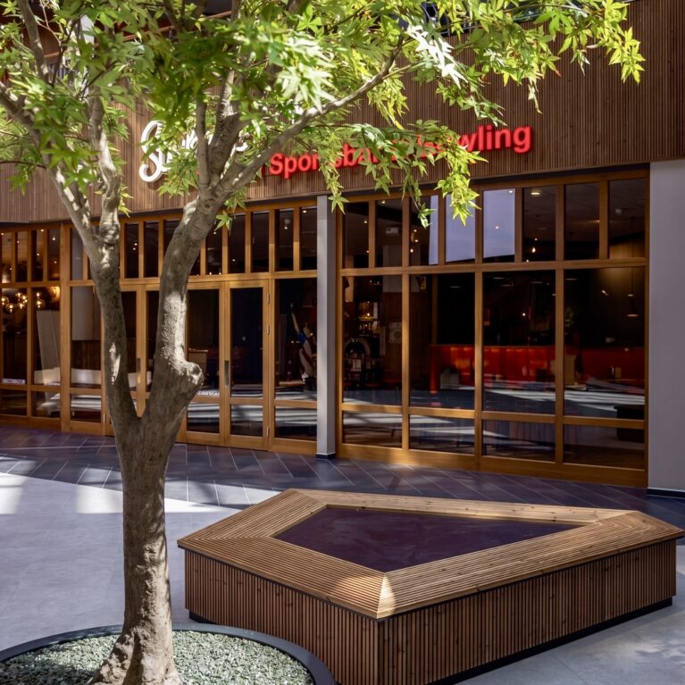 Custom timber bench, biophilic interior architecture, indoor tree planter, commercial plaza courtyard, timber frame storefront, hospitality rest zone, vertical wood slats, stone look tiling.