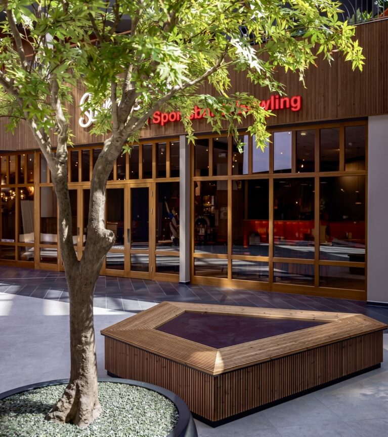 Custom timber bench, biophilic interior architecture, indoor tree planter, commercial plaza courtyard, timber frame storefront, hospitality rest zone, vertical wood slats, stone look tiling.