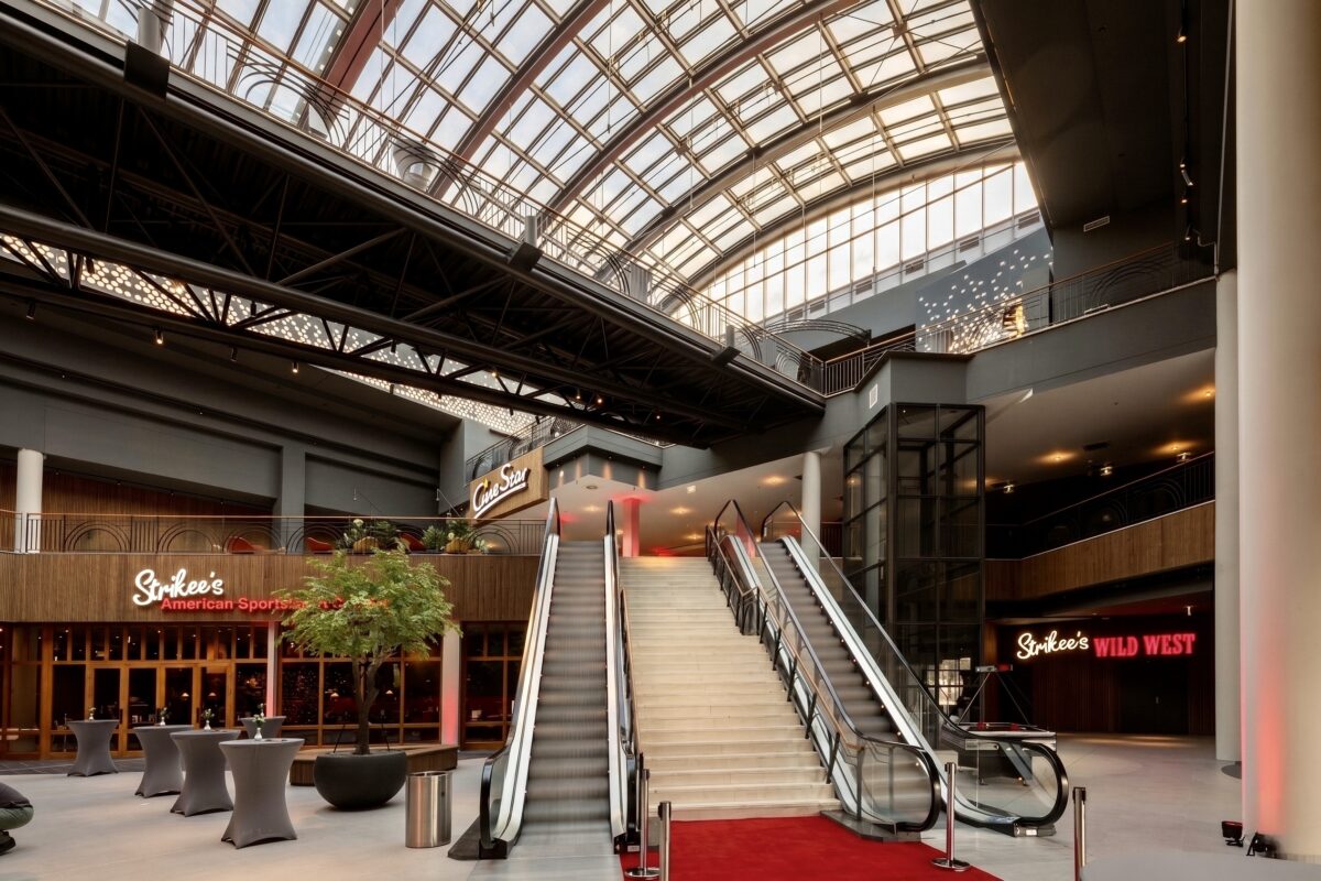 Commercial escalator installation, monumental foyer staircase, red carpet event entrance, glass barrel vault roof, structural steel beams, vertical wood cladding, commercial building atrium, restaurant facade design.