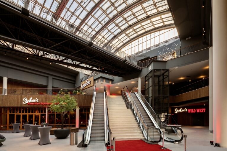 Commercial escalator installation, monumental foyer staircase, red carpet event entrance, glass barrel vault roof, structural steel beams, vertical wood cladding, commercial building atrium, restaurant facade design.