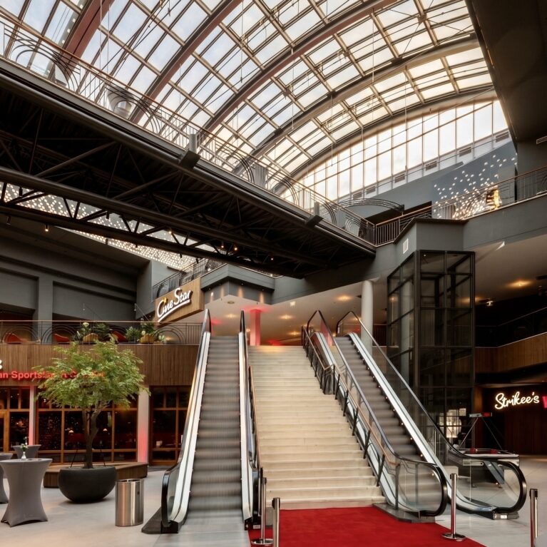 Commercial escalator installation, monumental foyer staircase, red carpet event entrance, glass barrel vault roof, structural steel beams, vertical wood cladding, commercial building atrium, restaurant facade design.