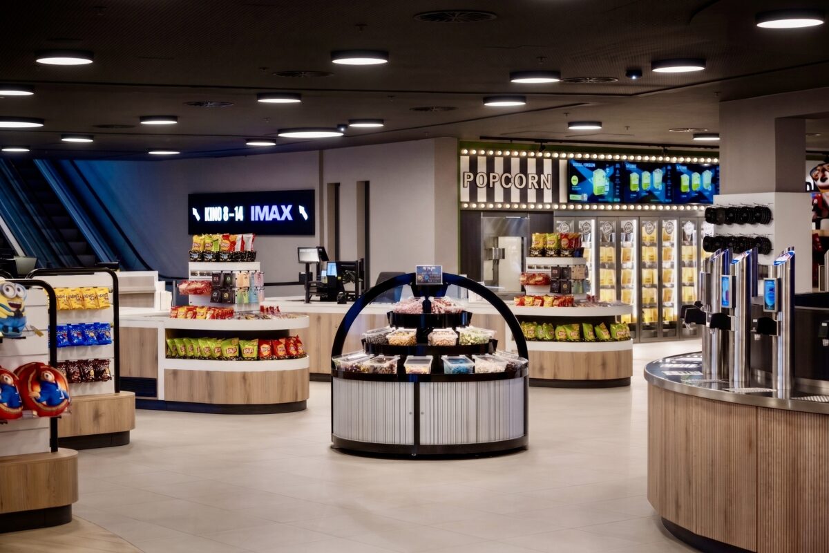 Cinema marketplace layout, retail display islands, concession stand design, timber clad counters, grab and go snack station, commercial pendant lighting, digital signage, theater concourse interior, terrazzo style flooring, modern box office retail.