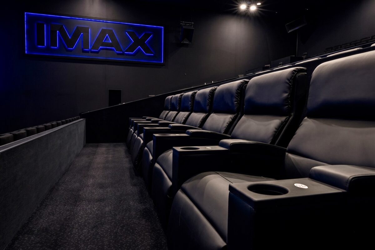 Premium cinema seating, luxury leather recliners, theater cup holders, deep pile carpet, matte black acoustic walls, neon auditorium signage, commercial theater fit-out, upscale stadium seating, ergonomic movie lounge chairs, dark interior finishes.
