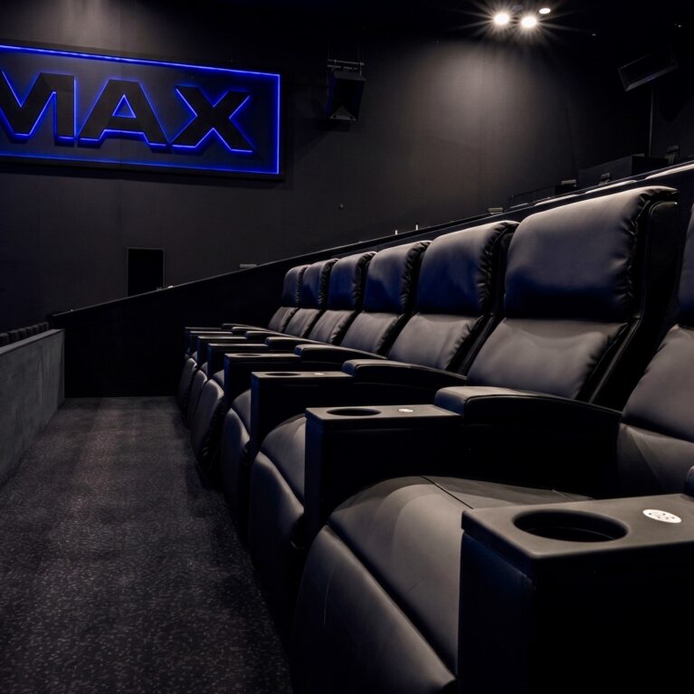 Premium cinema seating, luxury leather recliners, theater cup holders, deep pile carpet, matte black acoustic walls, neon auditorium signage, commercial theater fit-out, upscale stadium seating, ergonomic movie lounge chairs, dark interior finishes.