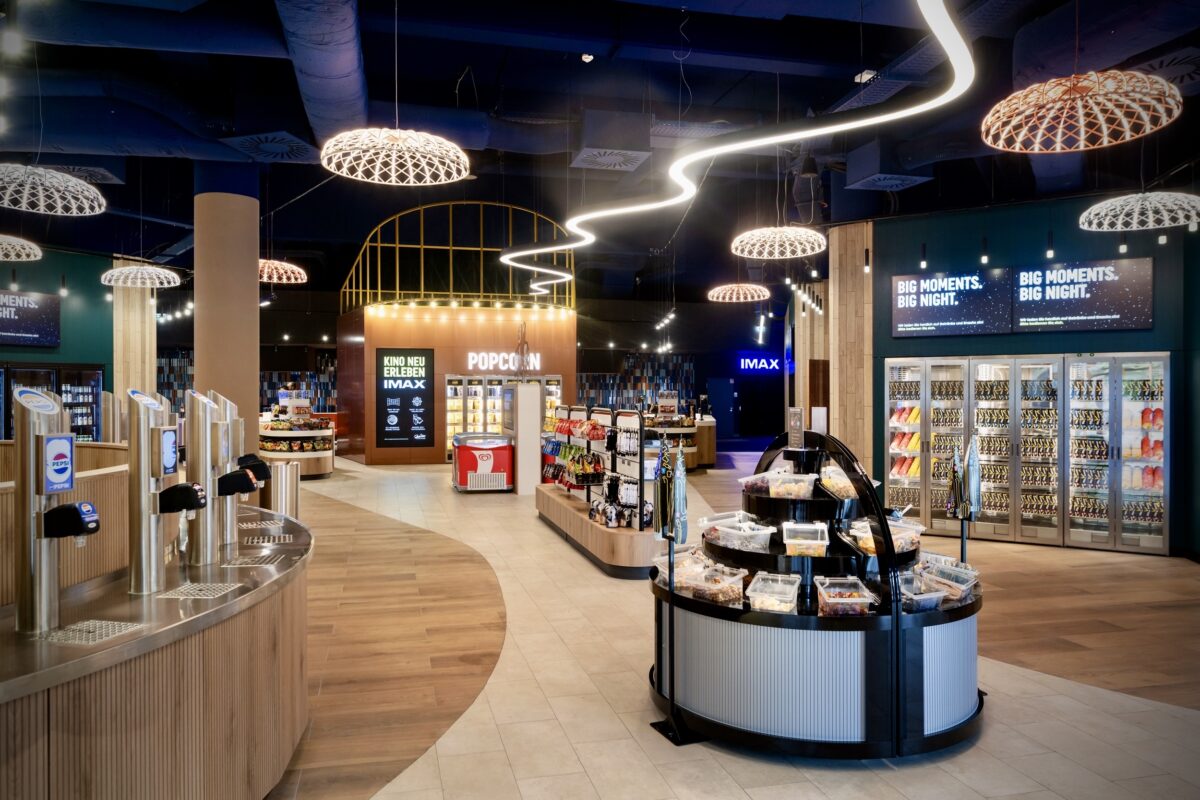 Self service beverage taps, woven pendant light domes, organic wave neon strip, timber slat counter, glass front warming cabinets, circular candy island, vinyl plank flooring, digital menu screens, retail concession layout