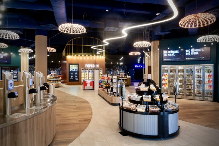 Self service beverage taps, woven pendant light domes, organic wave neon strip, timber slat counter, glass front warming cabinets, circular candy island, vinyl plank flooring, digital menu screens, retail concession layout