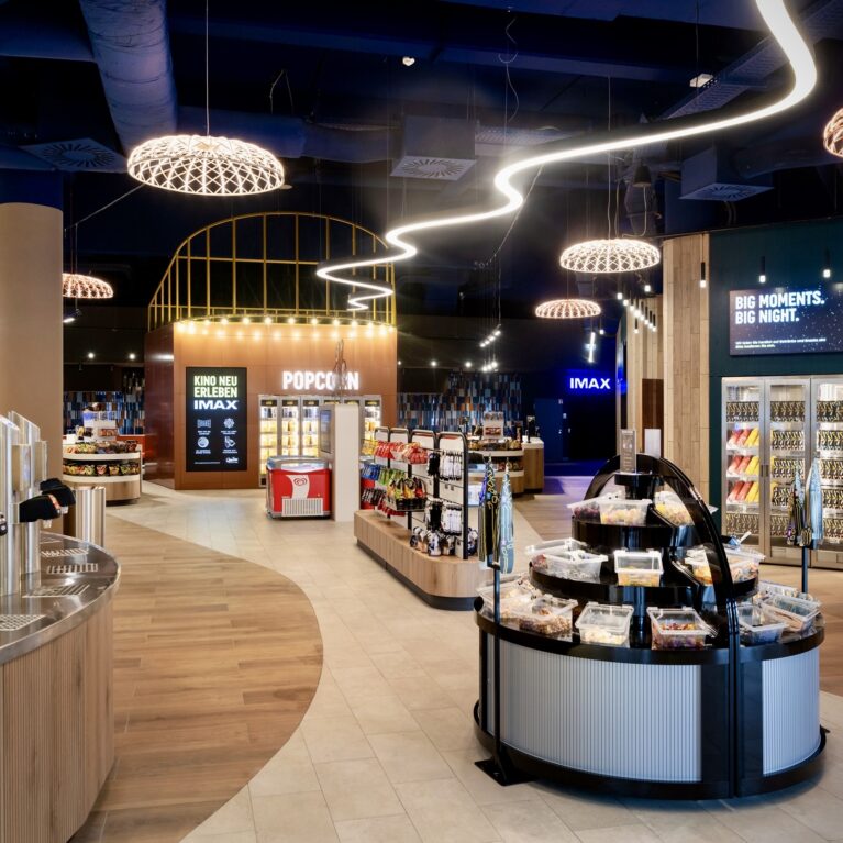 Self service beverage taps, woven pendant light domes, organic wave neon strip, timber slat counter, glass front warming cabinets, circular candy island, vinyl plank flooring, digital menu screens, retail concession layout
