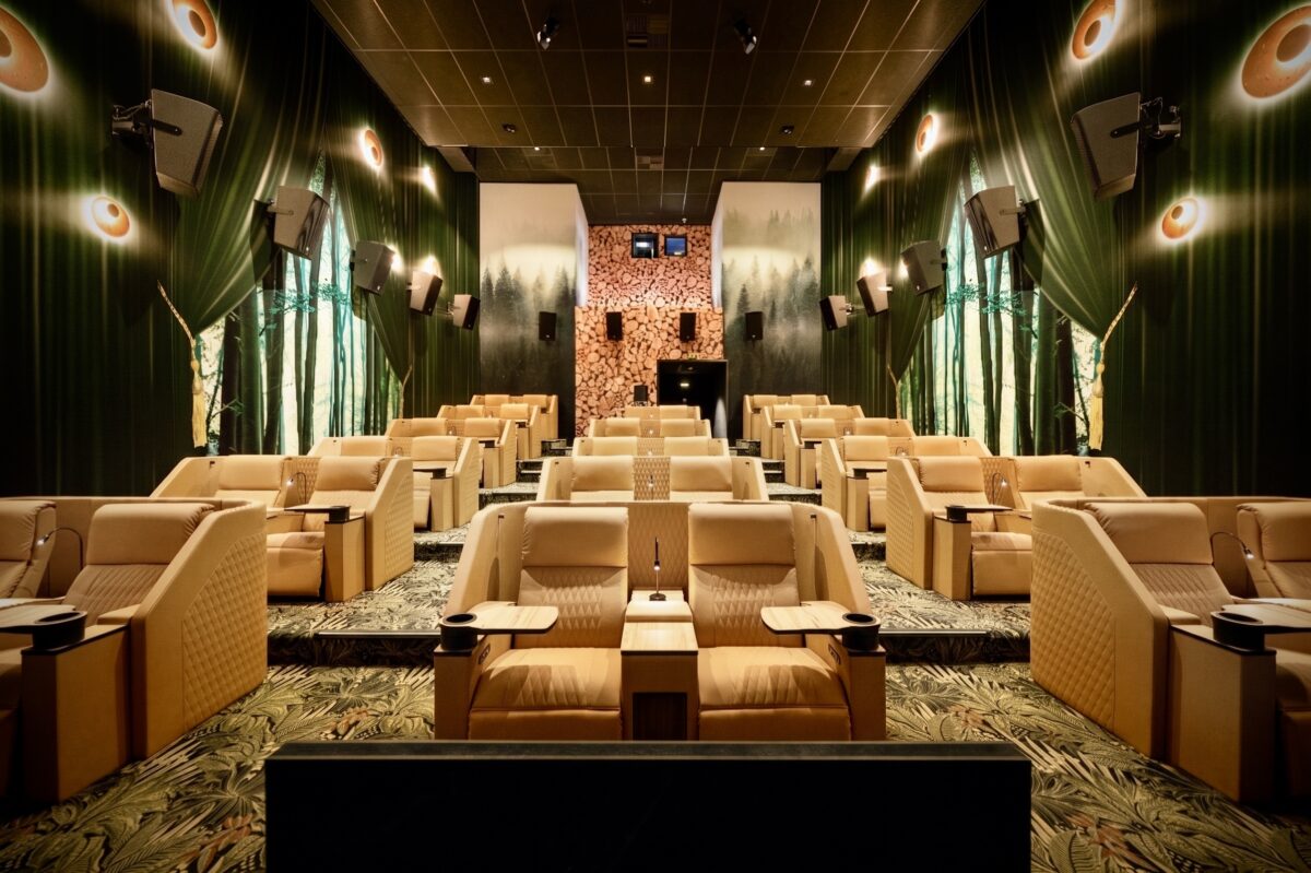 Beige quilted leather recliners, botanical patterned carpet, forest wall mural, timber log accent wall, directional seat lamps, surround sound speakers, tiered boutique auditorium, warm ambient sconces