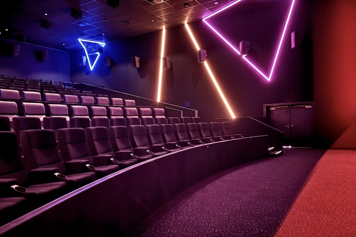 Geometric neon wall lights, linear LED accent strips, stadium cinema seating, black acoustic wall panels, surround sound wall speakers, red walkway carpet, curved barrier wall, large format auditorium layout