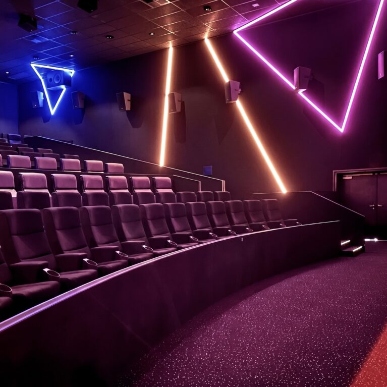 Geometric neon wall lights, linear LED accent strips, stadium cinema seating, black acoustic wall panels, surround sound wall speakers, red walkway carpet, curved barrier wall, large format auditorium layout