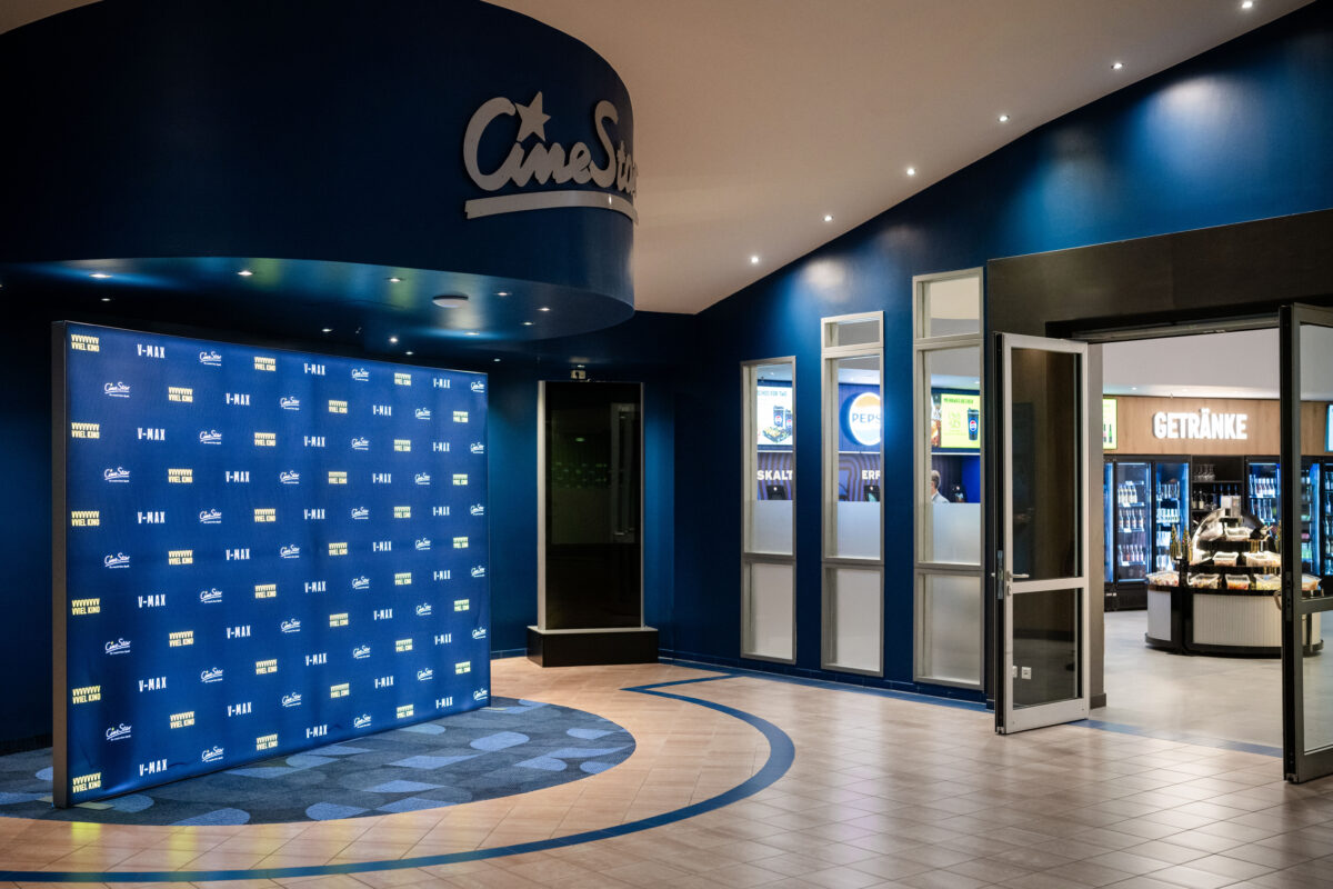 Step-and-repeat backdrop, curved architectural bulkhead, commercial entrance portal, interior glazing, porcelain floor tile, inset patterned carpet, recessed spotlighting, cinema foyer fit-out, retail marketplace entrance