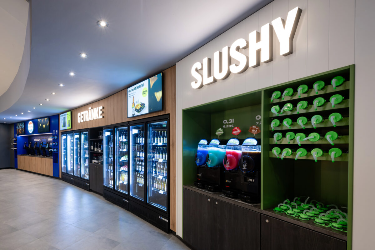 Self-service beverage wall, slush machine station, custom cup display rack, glass door reach-in coolers, digital menu monitors, illuminated channel lettering, vertical wall paneling, retail joinery fit-out, recessed ceiling spots