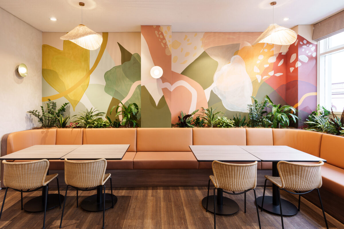 Custom painted mural wall, terracotta leather upholstery, woven rattan dining chairs, integrated planter box, biophilic interior design, woven shade pendant lamps, brass sconce lighting, continuous banquette bench, Sunshine Room fit-out