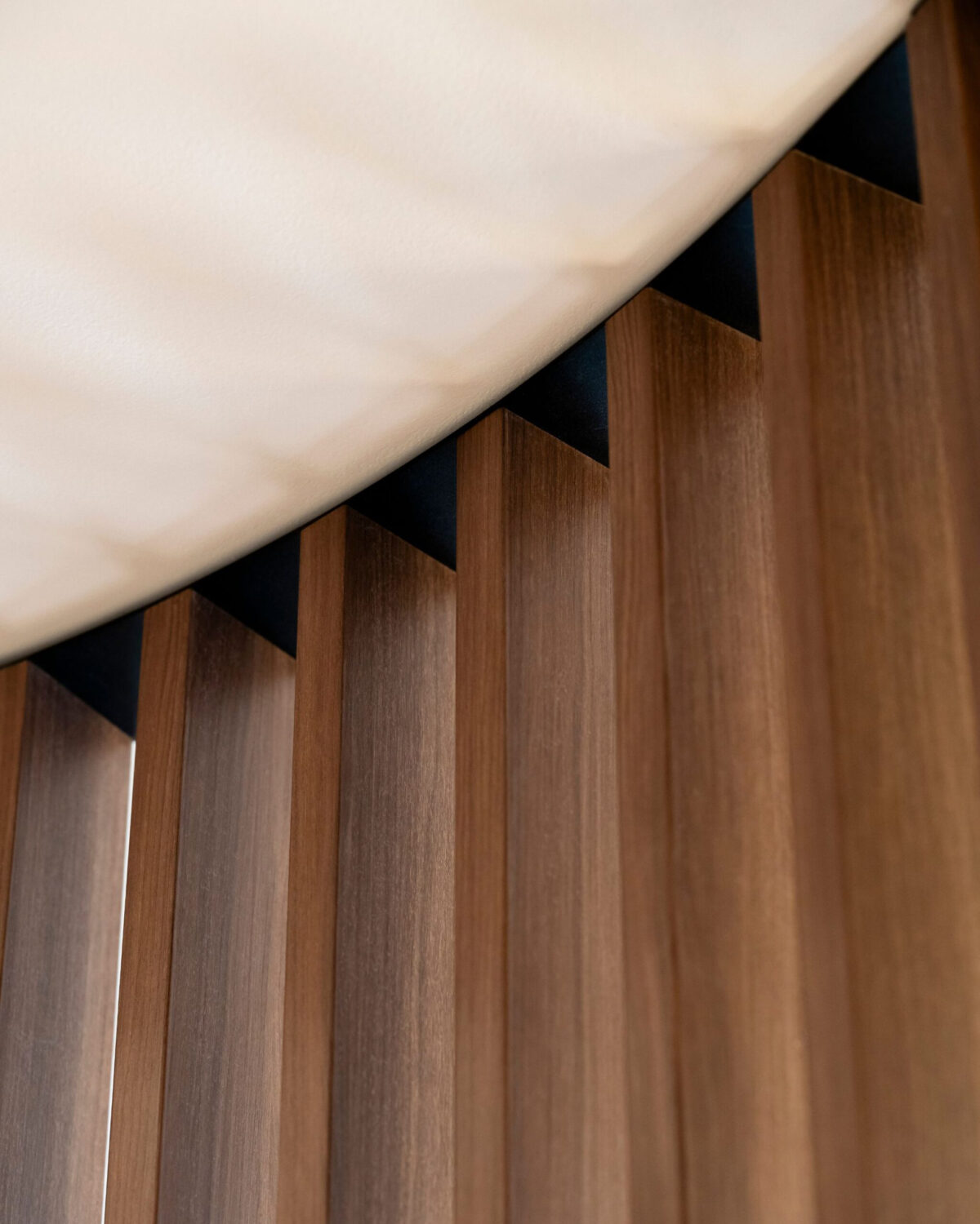 Vertical timber battens, shadow line reveal, ceiling junction, architectural millwork, wood grain texture, linear cladding, custom joinery detail, commercial ceiling interface, timber slat partition