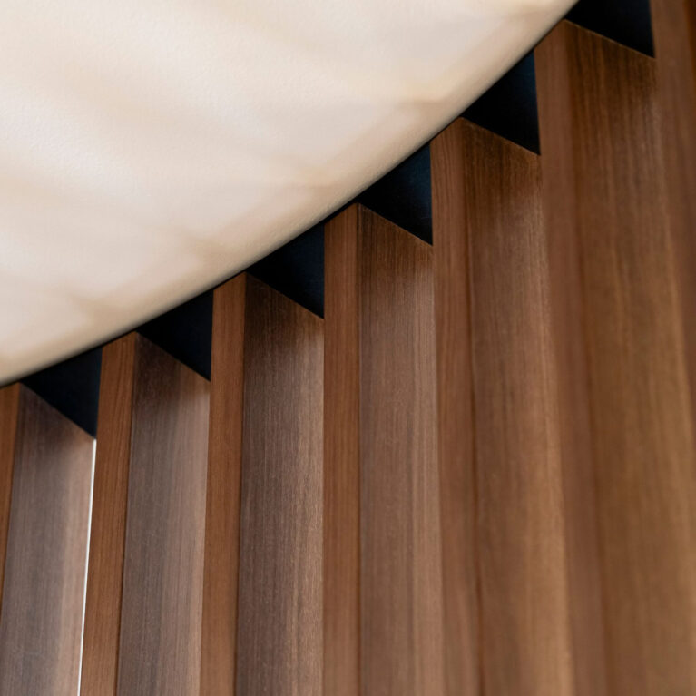 Vertical timber battens, shadow line reveal, ceiling junction, architectural millwork, wood grain texture, linear cladding, custom joinery detail, commercial ceiling interface, timber slat partition