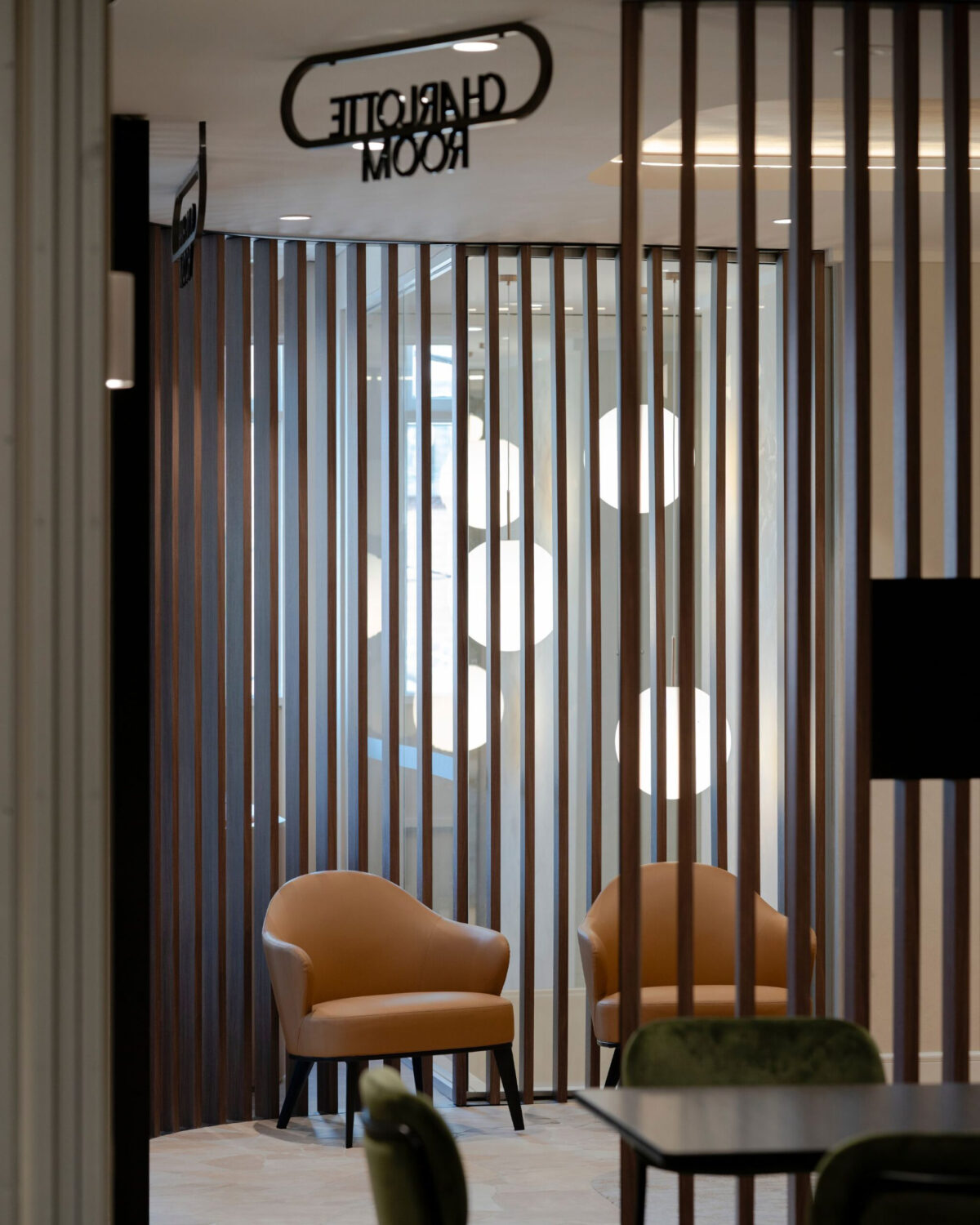 Vertical timber battens, cognac leather armchairs, acoustic timber partition, lounge nook seating, metal signage, globe pendant lighting, crazy paving stone flooring, club lounge design, venue foyer fit-out