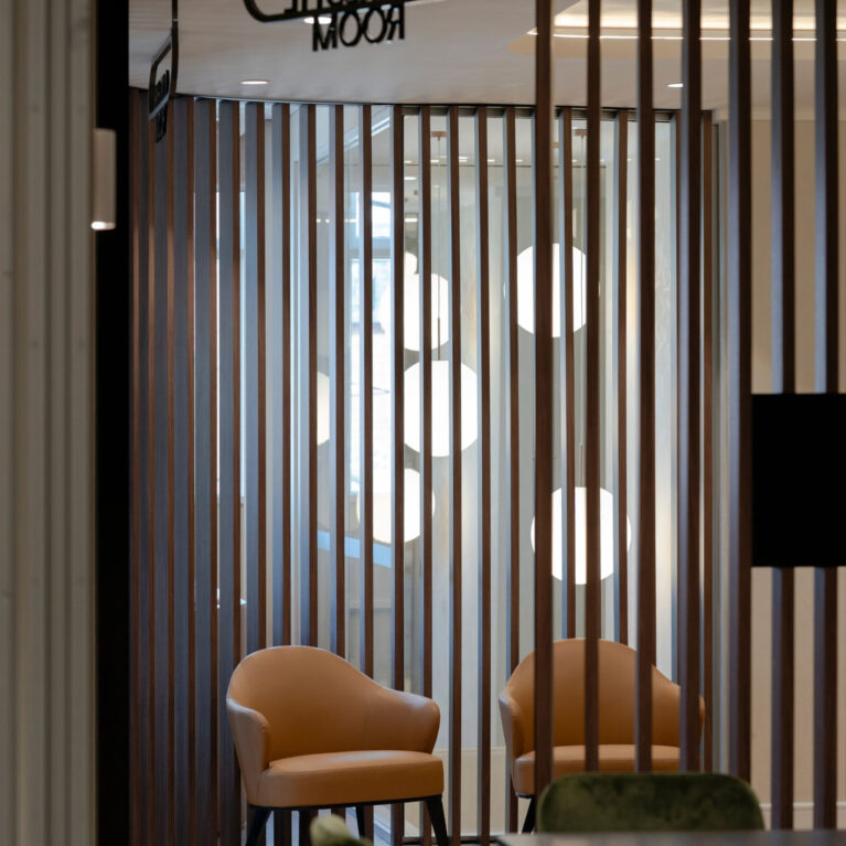Vertical timber battens, cognac leather armchairs, acoustic timber partition, lounge nook seating, metal signage, globe pendant lighting, crazy paving stone flooring, club lounge design, venue foyer fit-out