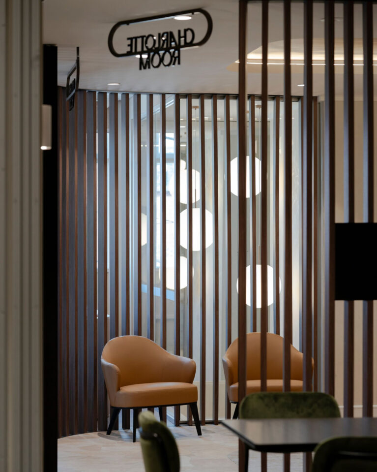 Vertical timber battens, cognac leather armchairs, acoustic timber partition, lounge nook seating, metal signage, globe pendant lighting, crazy paving stone flooring, club lounge design, venue foyer fit-out