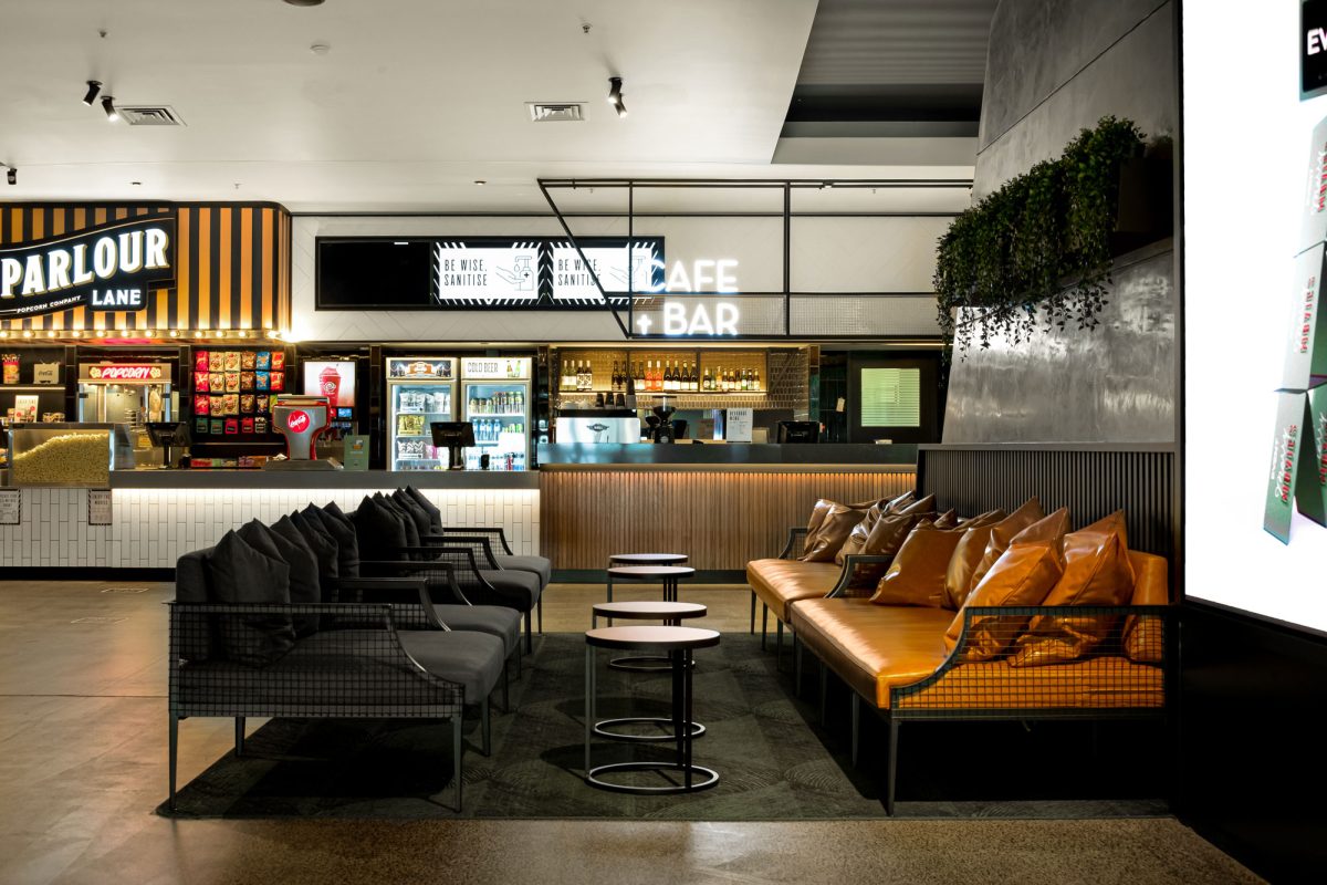 A stylish cafe lounge within the cinema, featuring comfortable seating, a modern bar counter, and warm wood tones.