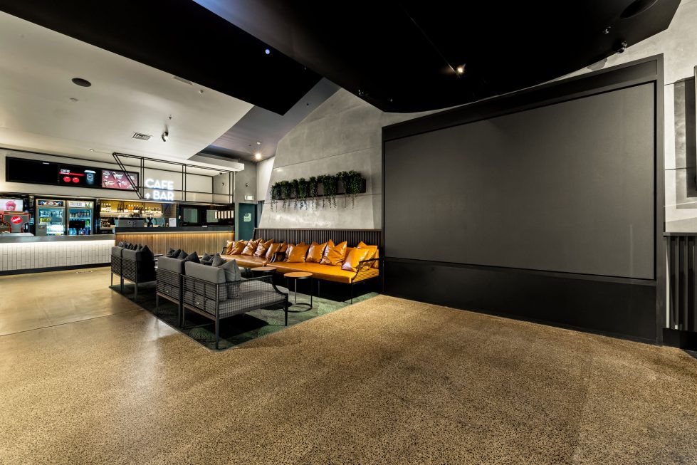 Cinema lobby with a large screen for movie trailers, comfortable seating, and modern decor.