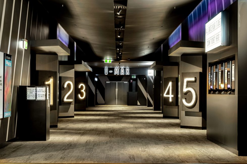 A sophisticated cinema concourse with modern design elements and illuminated theater numbering.