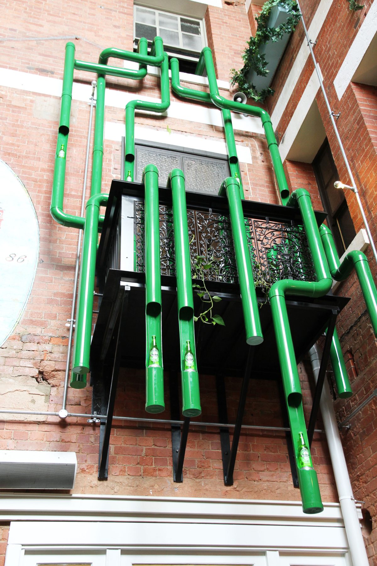 Multi-level hospitality installation, architectural brick facade, green conduit network, suspended DJ balcony, product showcase pods, commercial pop-up design.