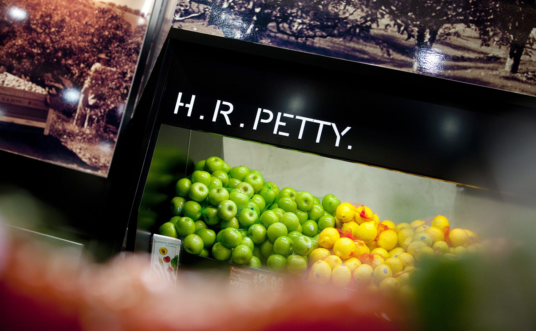 Fresh fruit display, black timber cabinetry, crisp brand lettering, heritage farm photos, color blocked green apples, fresh market merchandising, commercial spot lighting.
