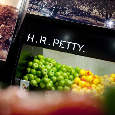 Fresh fruit display, black timber cabinetry, crisp brand lettering, heritage farm photos, color blocked green apples, fresh market merchandising, commercial spot lighting.